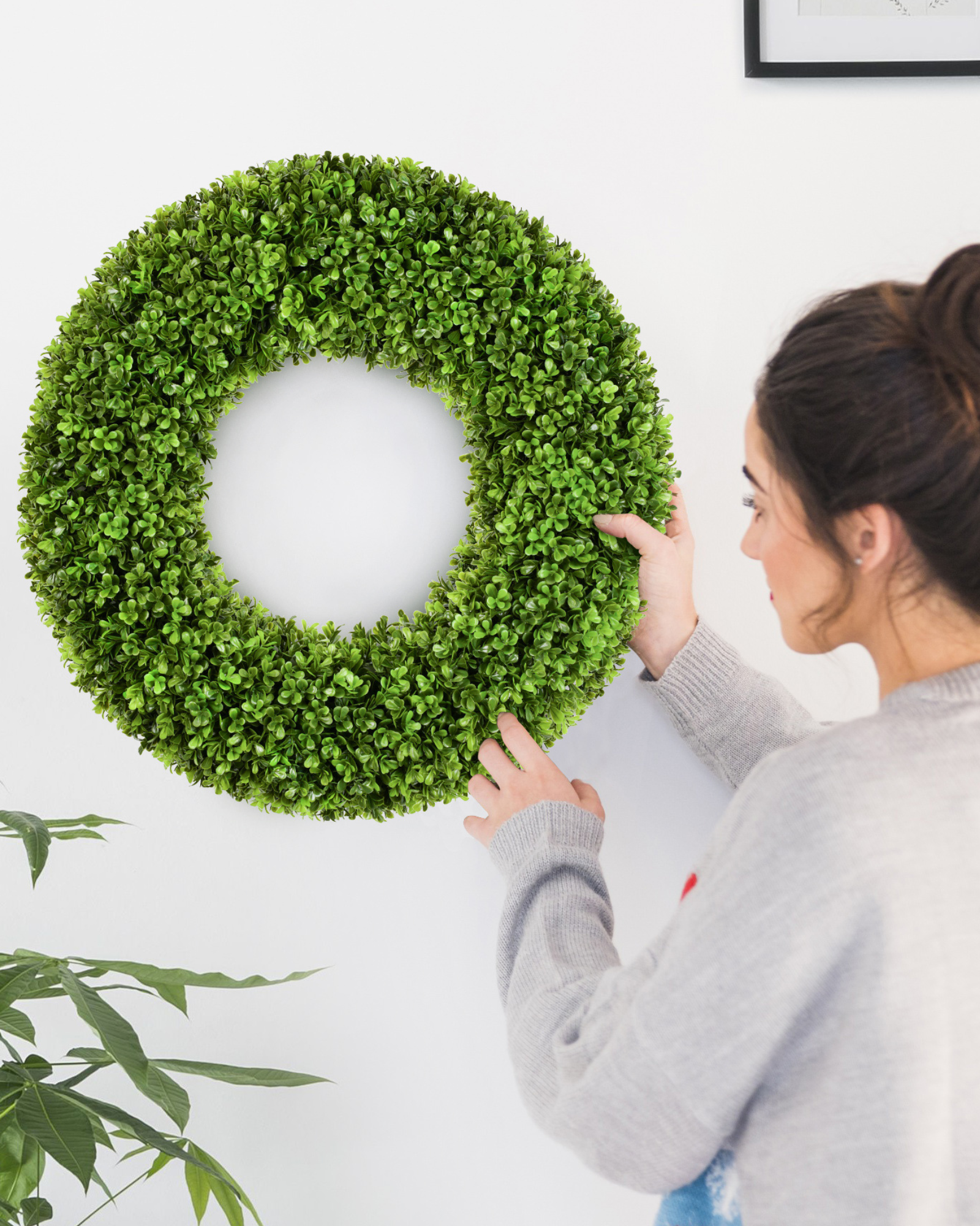A women is holding a 20 inch artificial boxwood wreath in the living room.